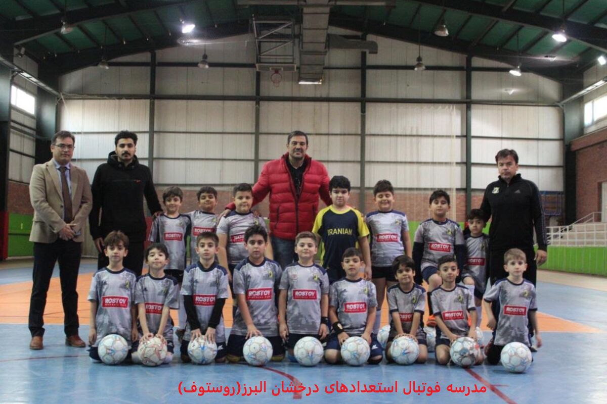عکس تیمی فوتبال آموزان نونهال با لباسهای طوسی و سورمه ای در سالن ورزشی به همراه مربیان خود
